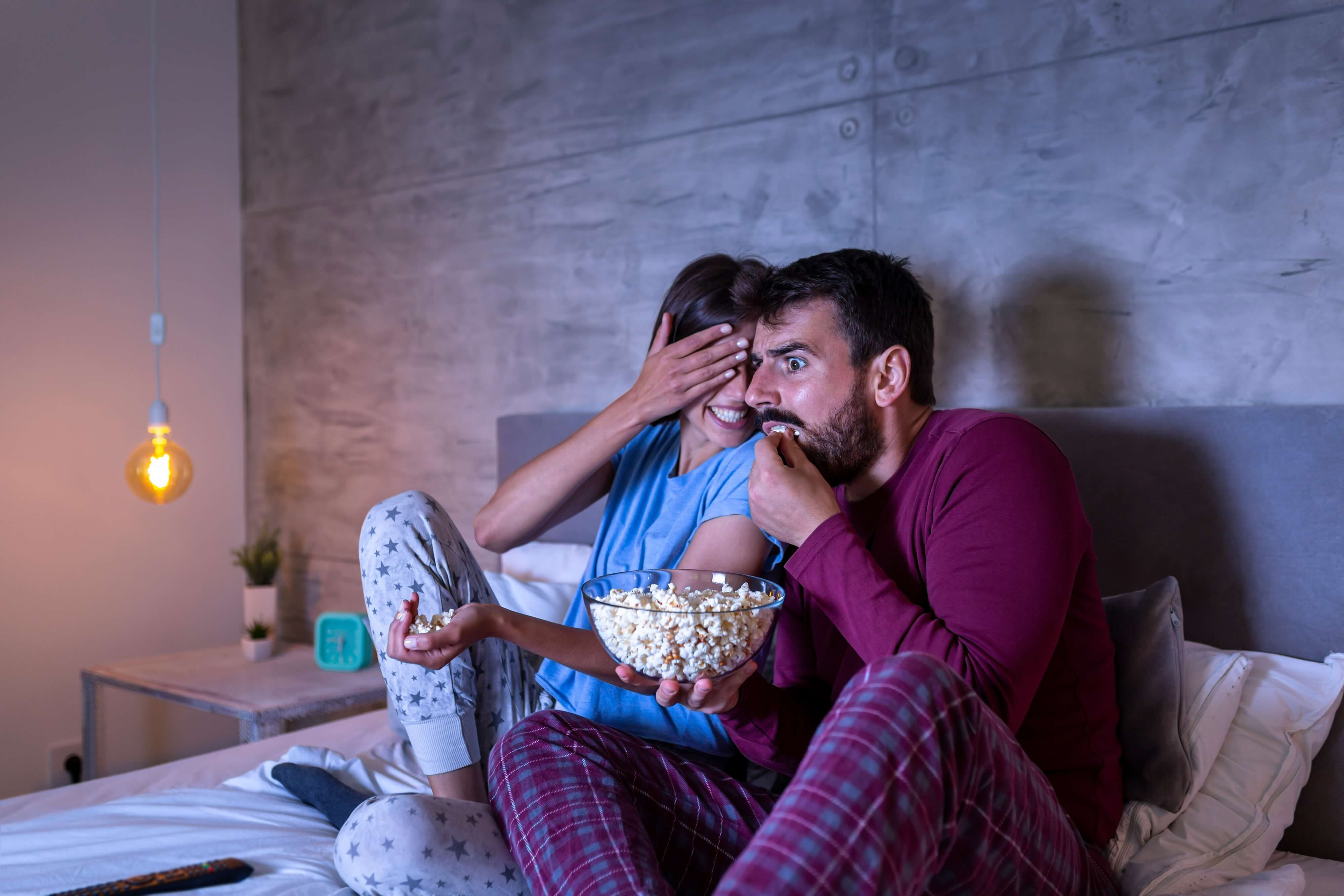 couple watching a horror movie in bed