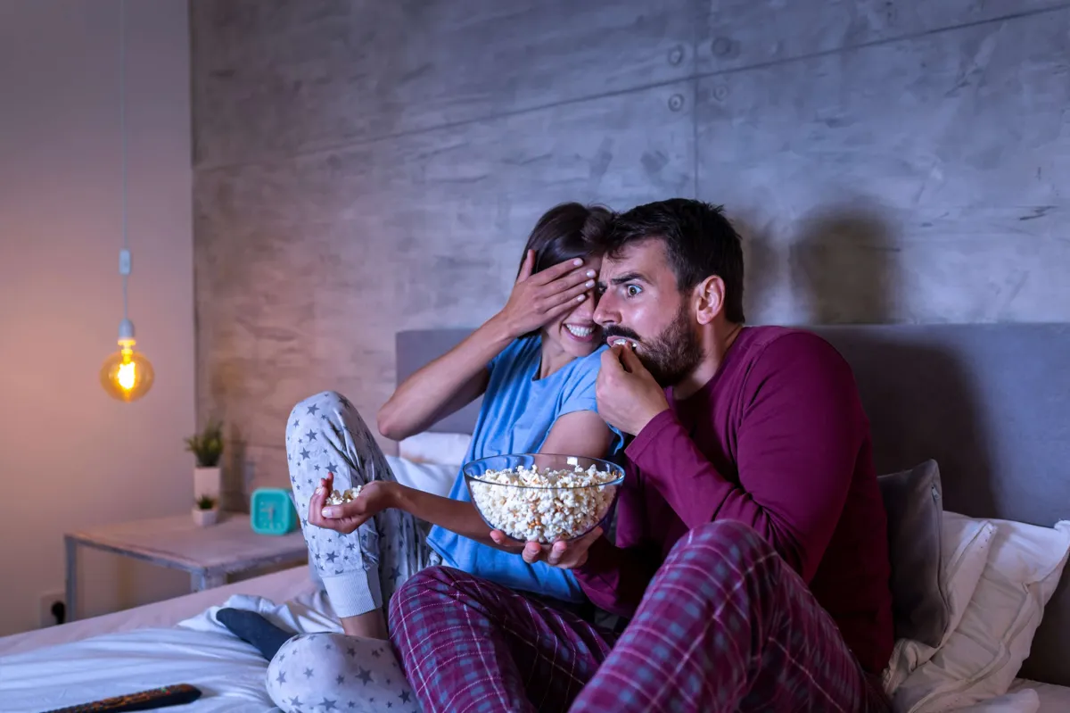 couple watching a horror movie in bed