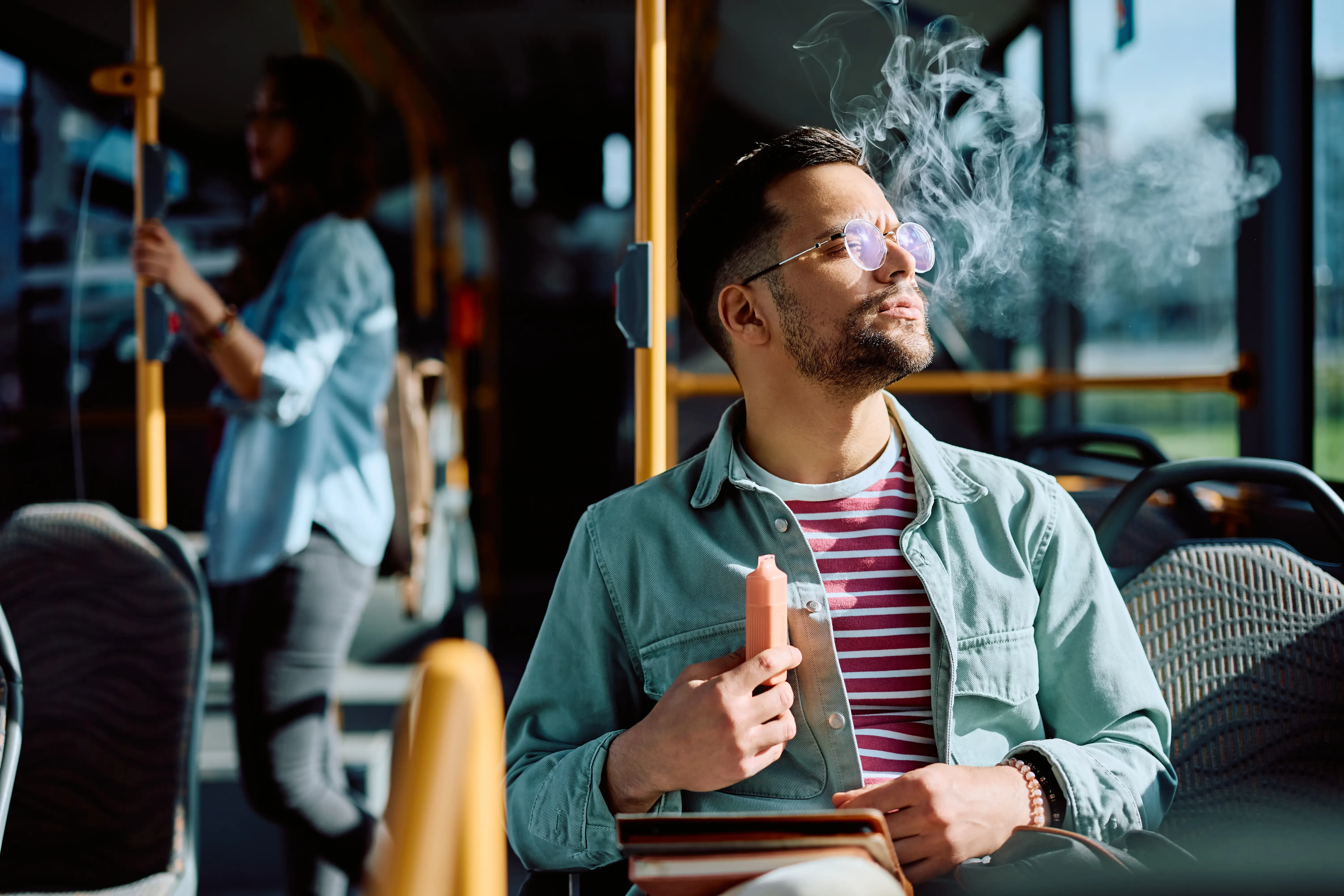 man using a disposable vape on a bus