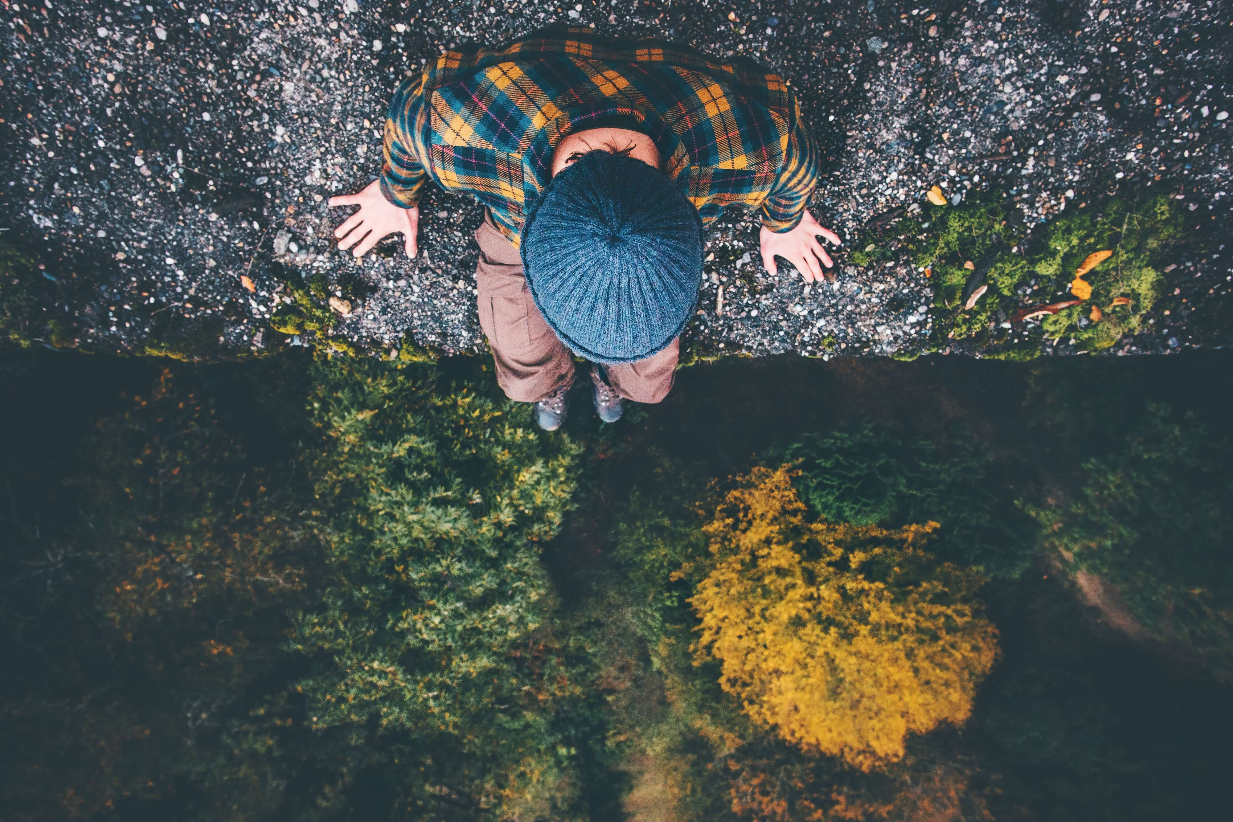 man looking at the edge of a cliff at nature below