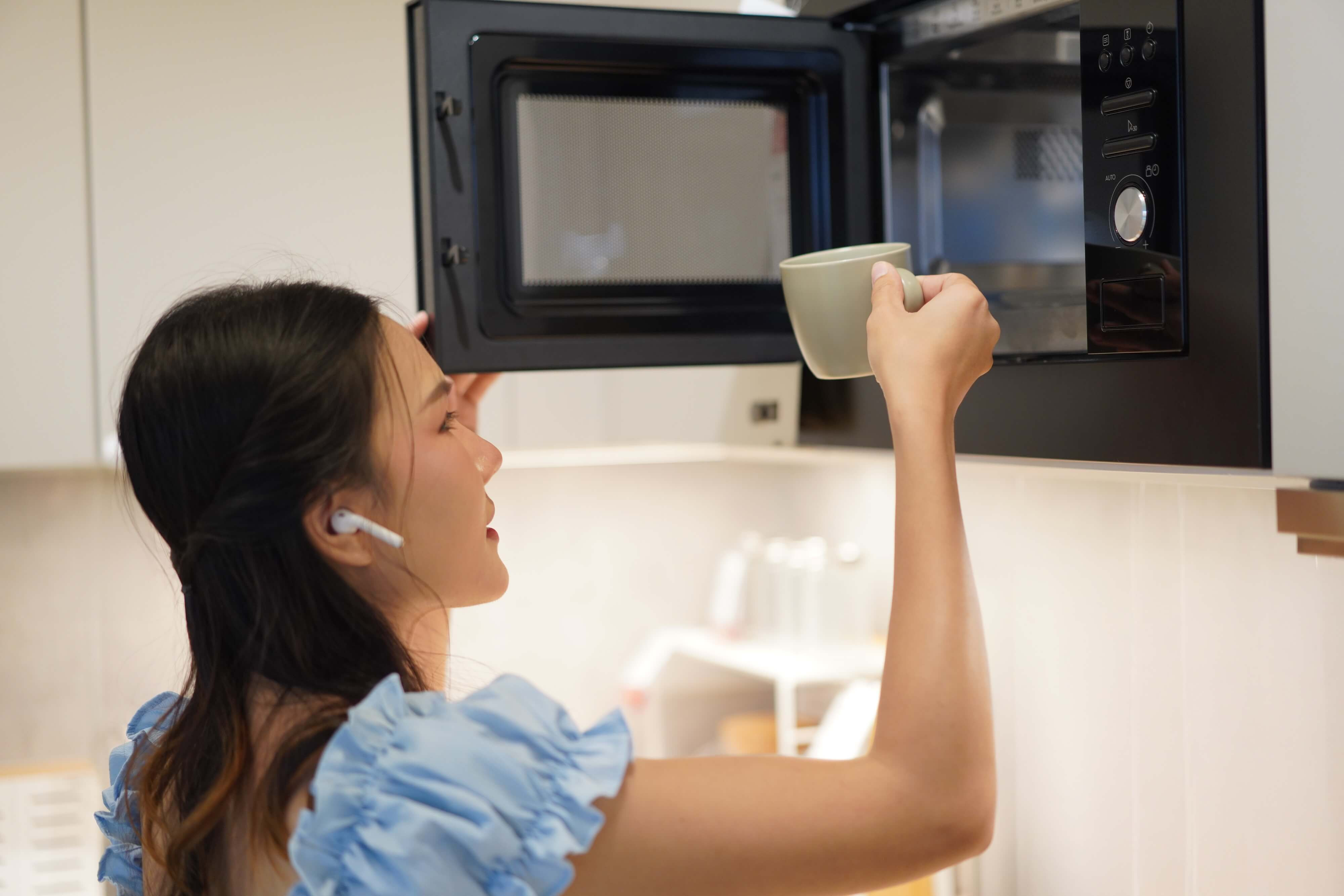 asian woman using microwave in kitchen